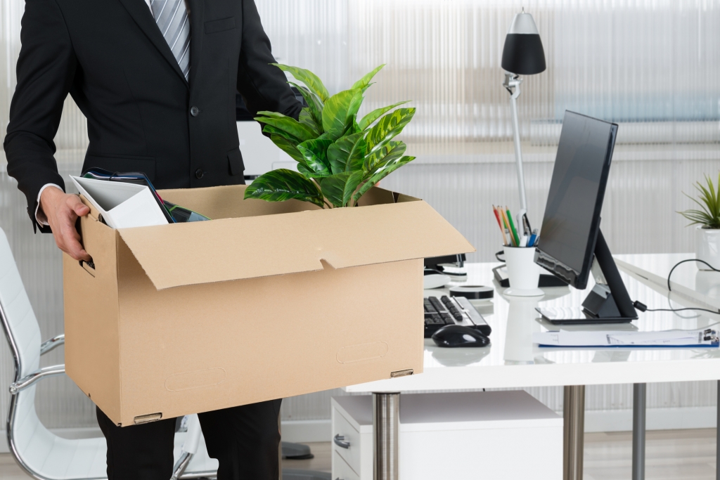 Midsection of businessman carrying cardboard box by desk in office