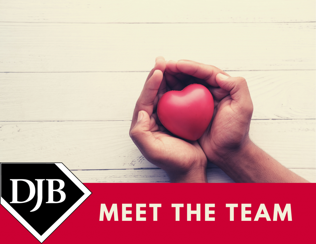A hand holding a red heart with a banner below - meet the team