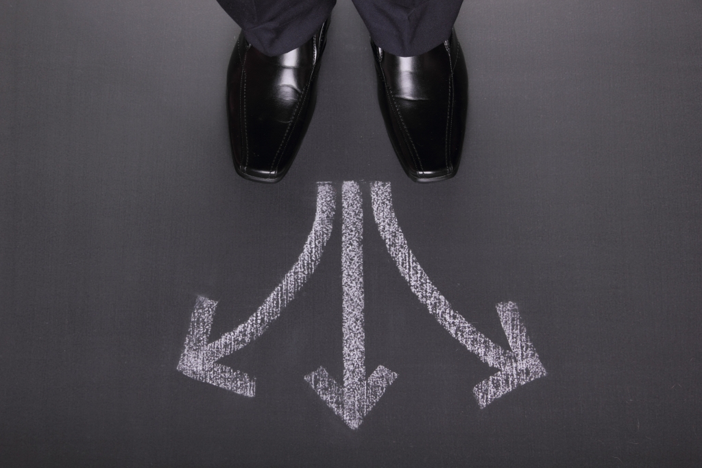 Unrecognizable businessman standing in front of three arrows showing different ways