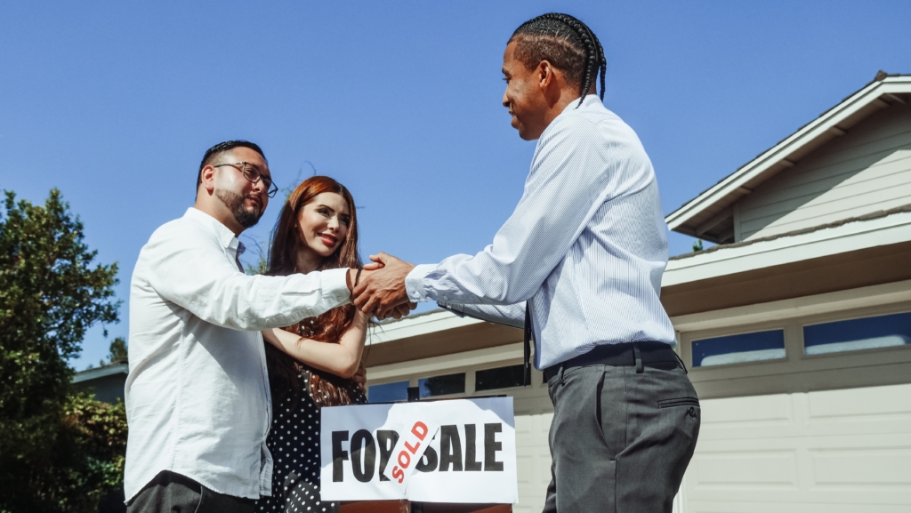 realtor shaking hand of clients in front of sold sign