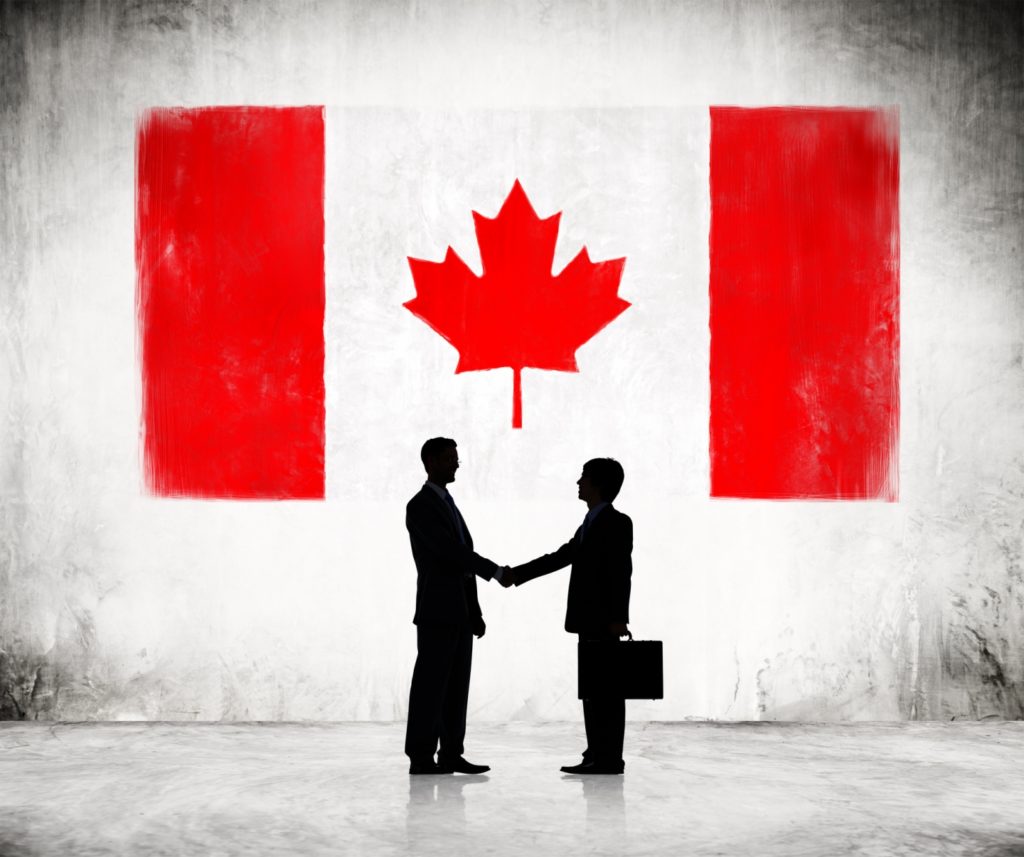 Two Businessmen Shaking Hands With Canadian Flag As A Background