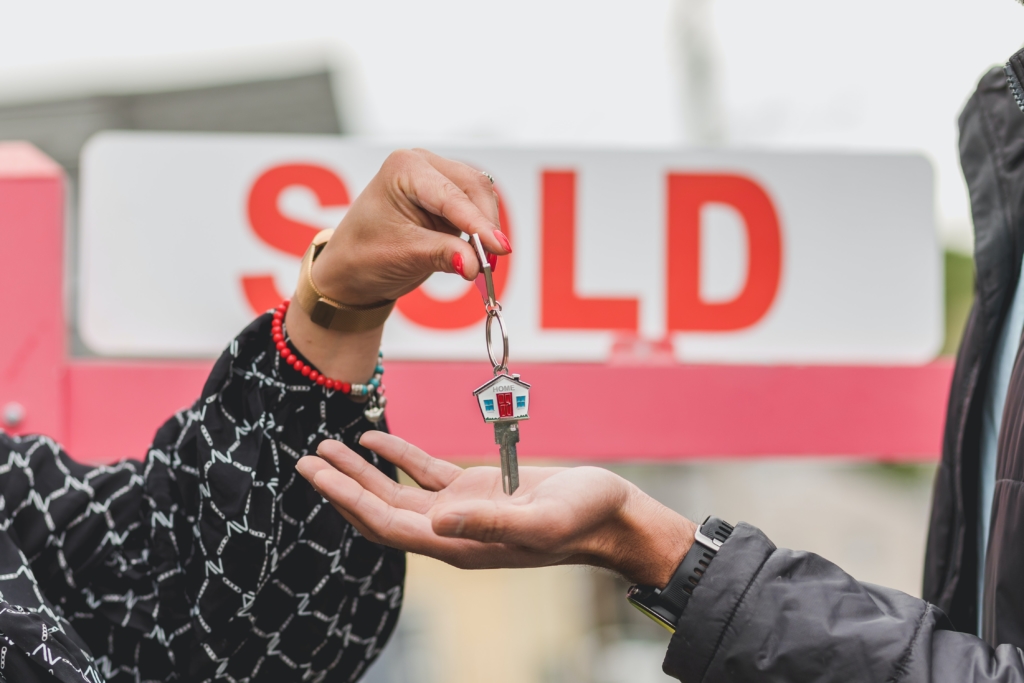 woman handing over keys for new home in front of a sold sign