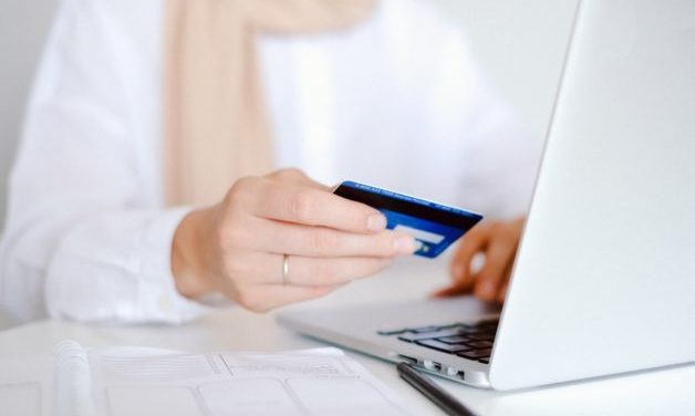 close up of person holding a credit card. Sitting in front of laptop