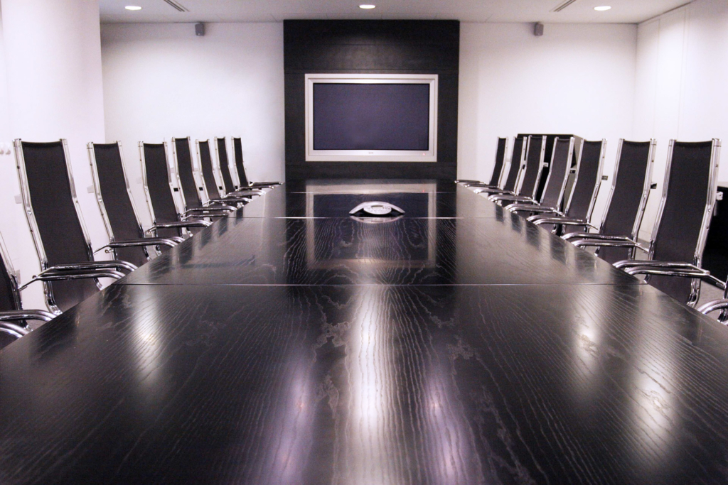 wooden boardroom table with black chairs around it. TV mounted on wall.