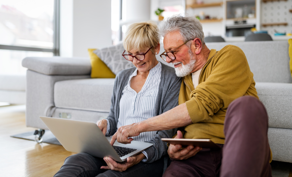 Cheerful happy senior couple using technology devices and having fun at home