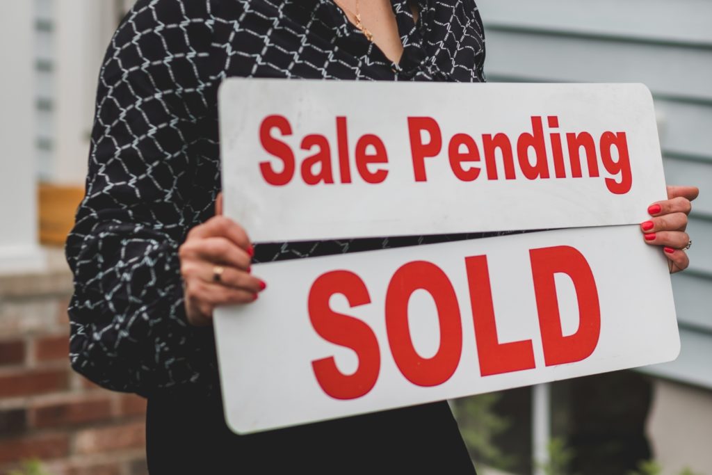 Close up of women holding a white sign with red lettering that reads "Sale Pending Sold"