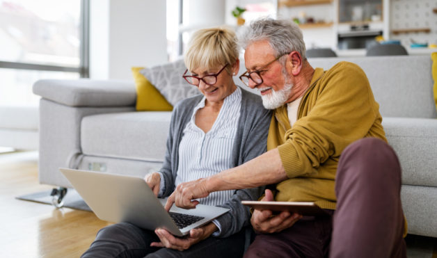 Cheerful happy senior couple using technology devices and having fun at home