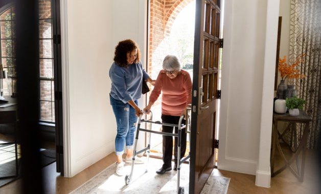 The mid adult woman helps her senior adult friend carefully enter her home.