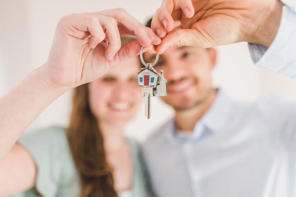 a young couple both dressed in blue, holding a key to their first home