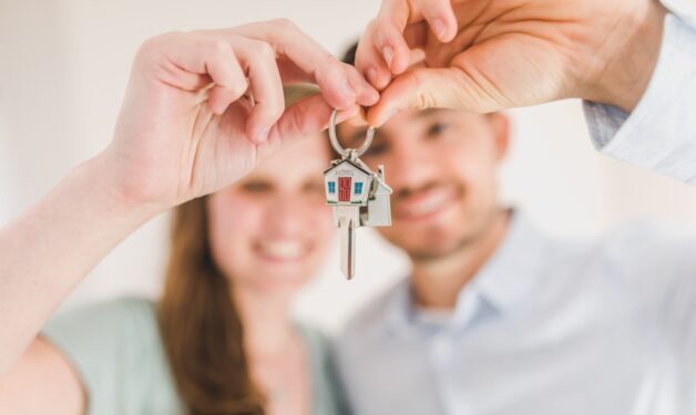 a young couple both dressed in blue, holding a key to their first home