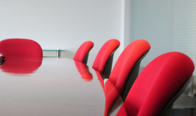 Meeting room. Close-up of corner of wood table with red chairs around it.
