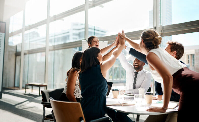 Shot of a group of businesspeople high fiving while sitting in a meeting