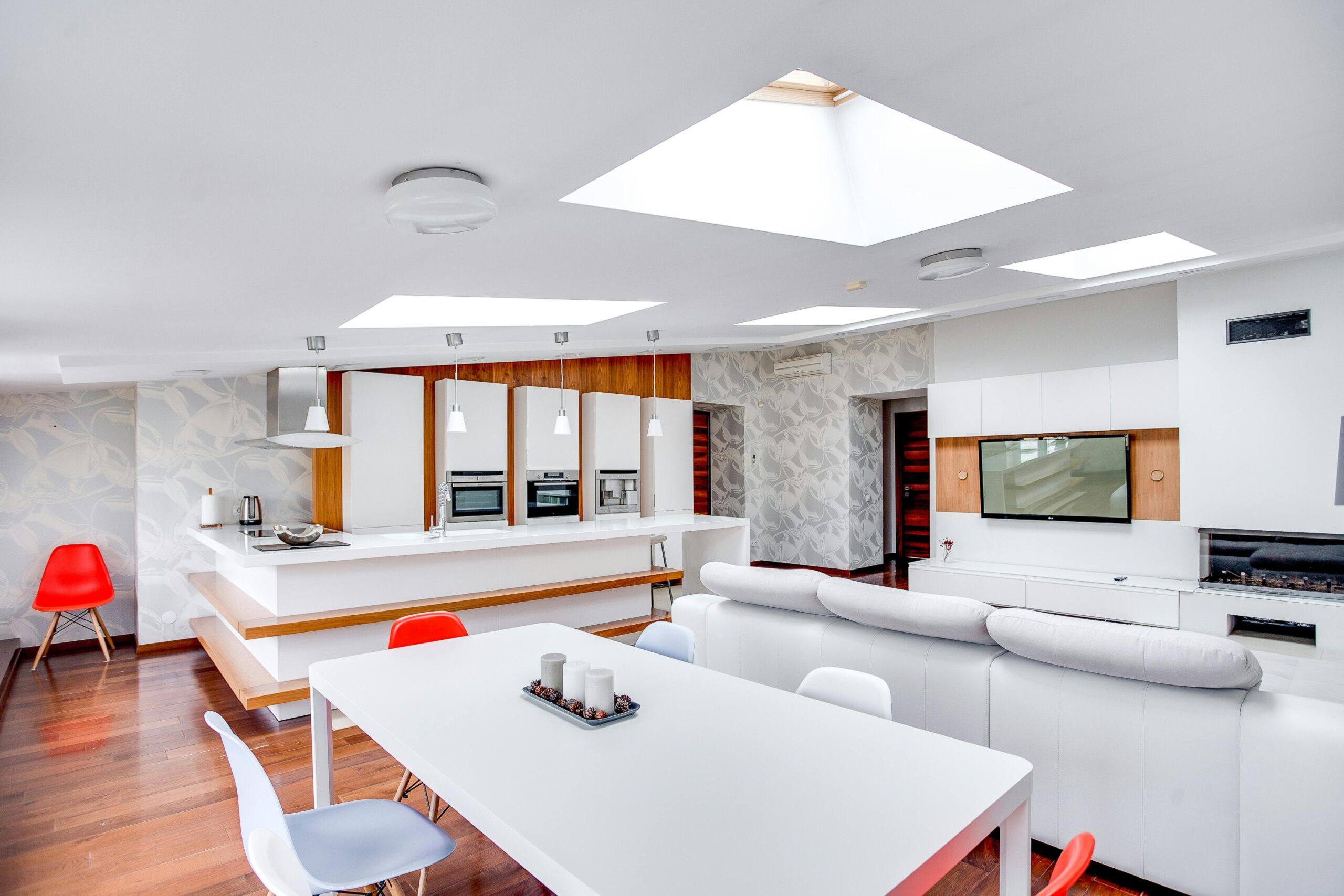Inside of an apartment building. Kitchen is white with a white table and red & white chairs.