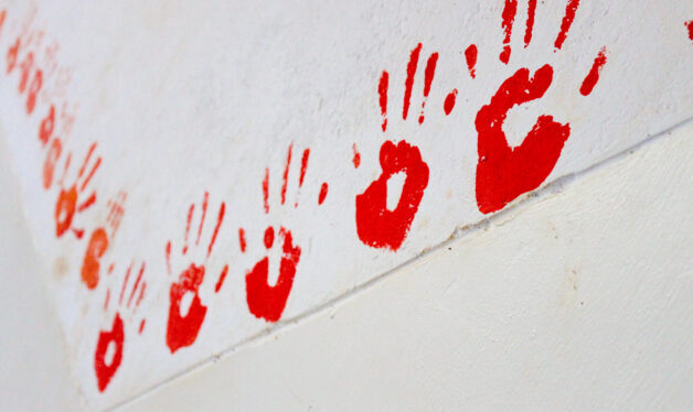 Picture of multiple red hand prints on a white wall.