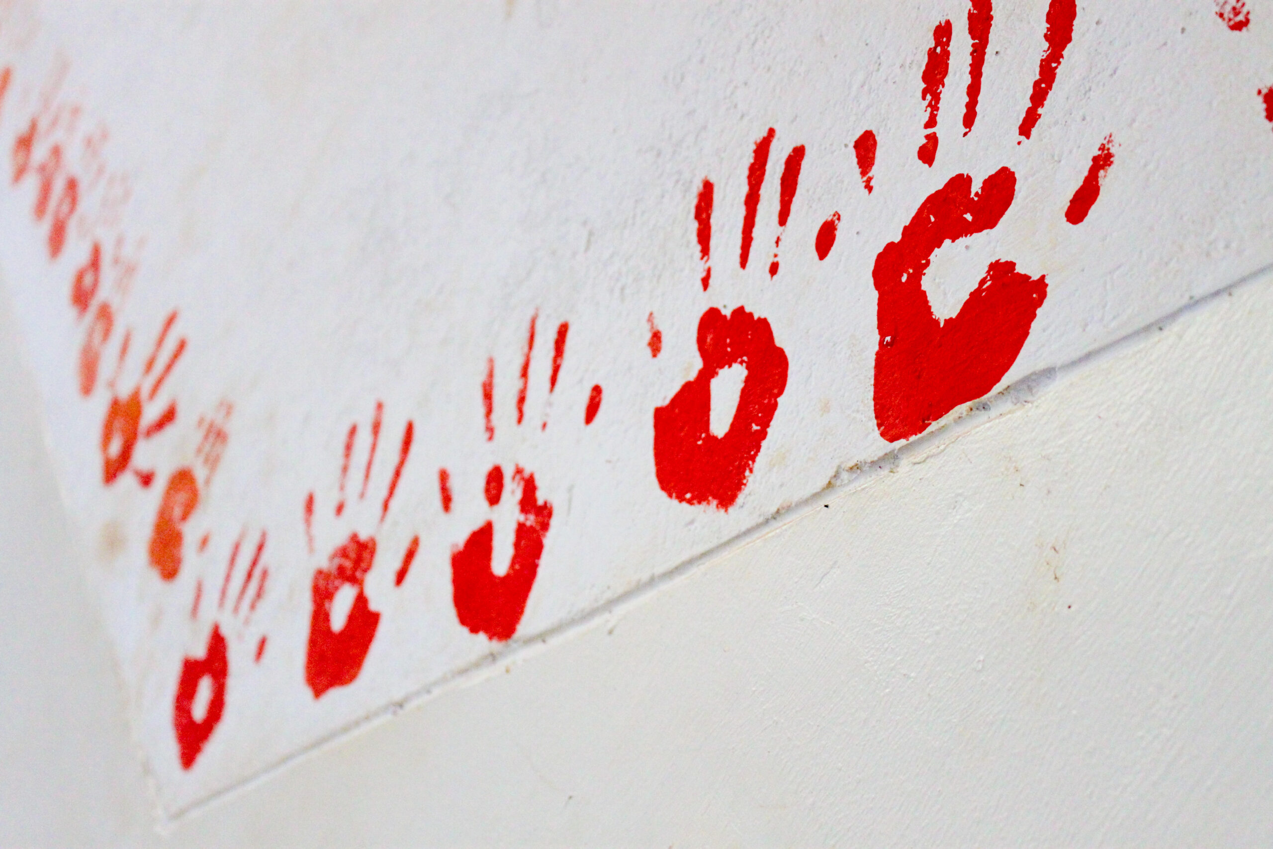 Picture of multiple red hand prints on a white wall.