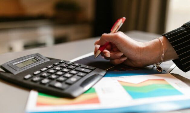 Business woman holding red pen with calculator beside her.