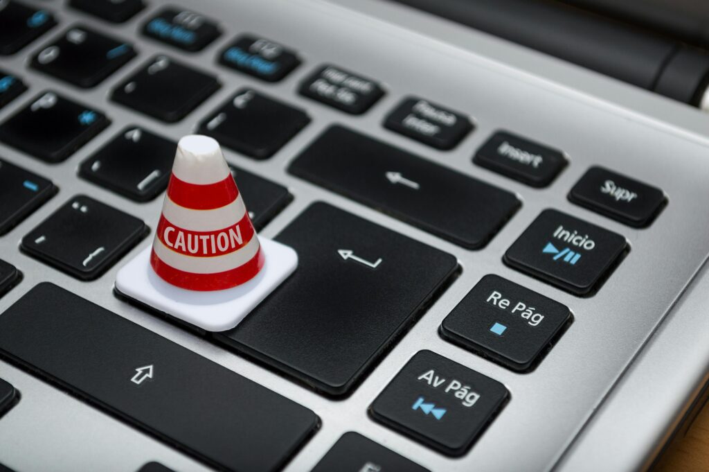 close up of laptop with a small pylon sitting on the keyboard. The pylon has the word caution on it