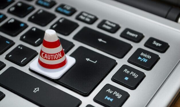 close up of laptop with a small pylon sitting on the keyboard. The pylon has the word caution on it