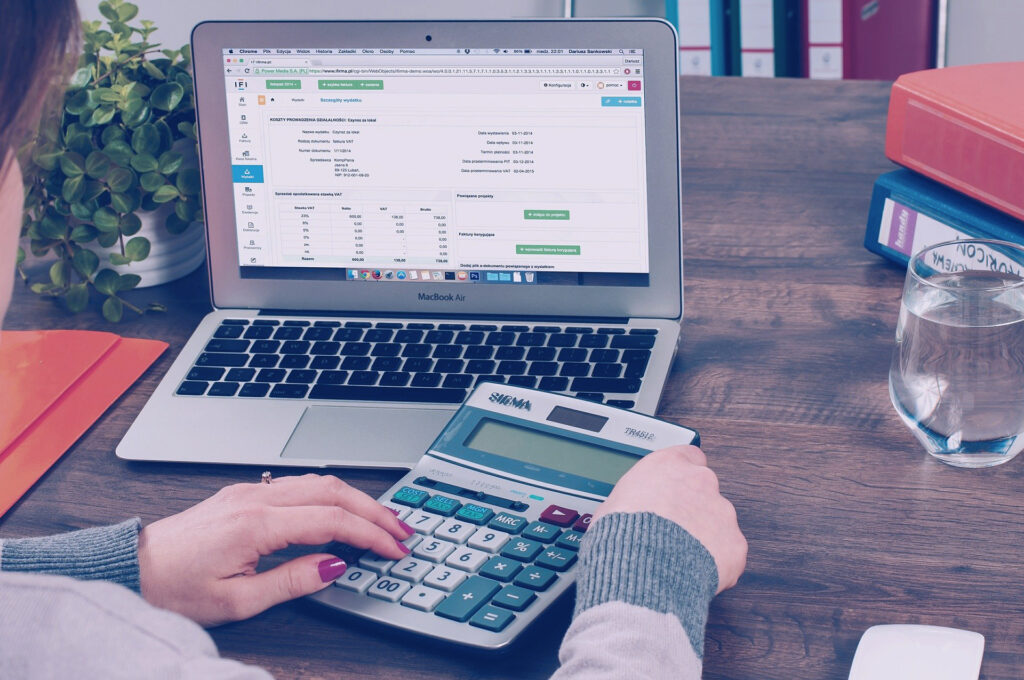 Laptop with numbers on the screen. Person sitting in front of the laptop, doing a calculation on a calculator.