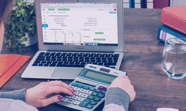 Laptop with numbers on the screen. Person sitting in front of the laptop, doing a calculation on a calculator.