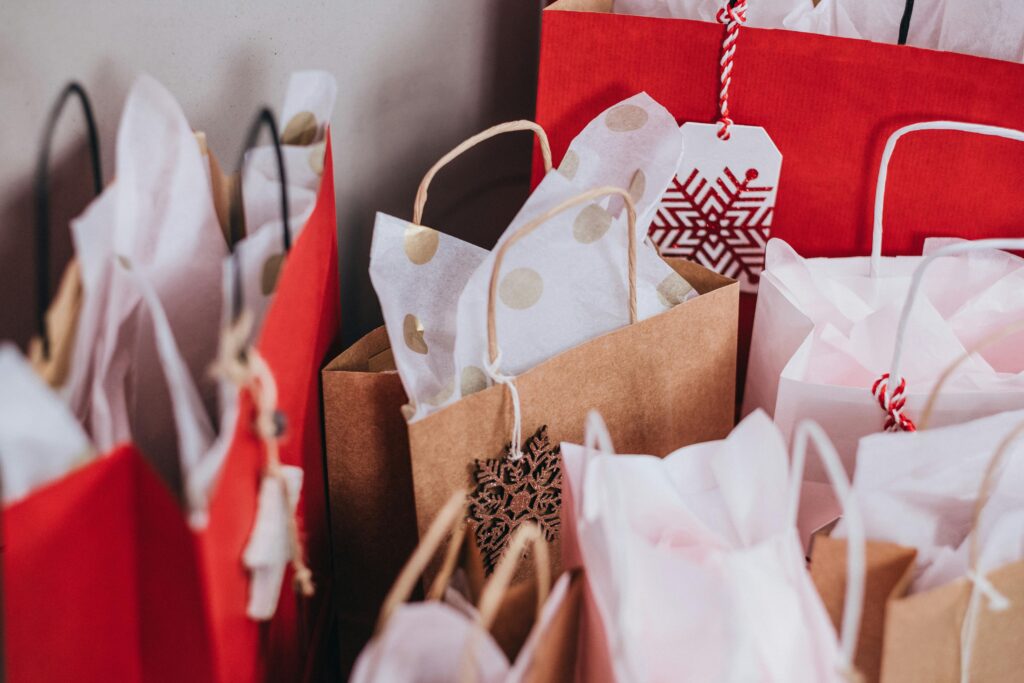 Close-up of numerous bags of presents. Some bags are red and some are paper bags. All bags have white tissue paper.