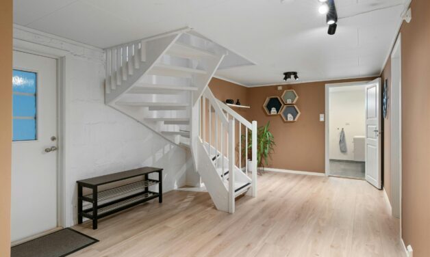 White winding stairs leading to basement apartment. White walls and hardwood floor. There is a bench against the wall.