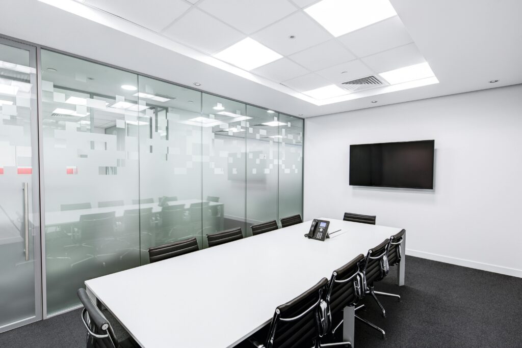 Empty boardroom. White table, black chairs, and a tv on the wall. One wall of the boardroom is made of glass.