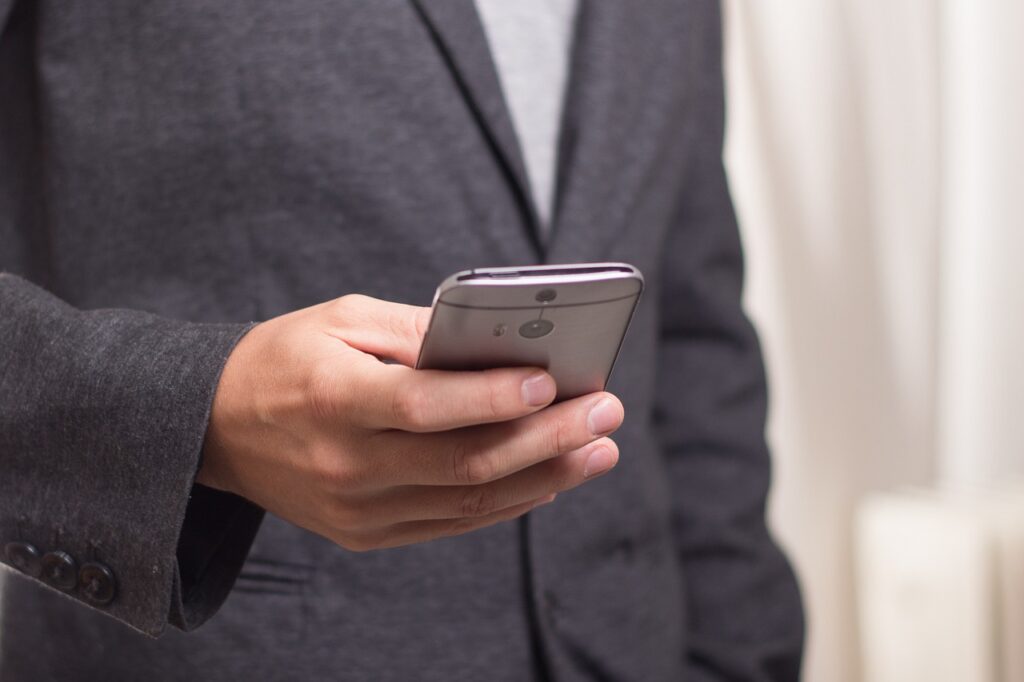 Photo of man in gray suit holding a cell phone. Close up of hand.