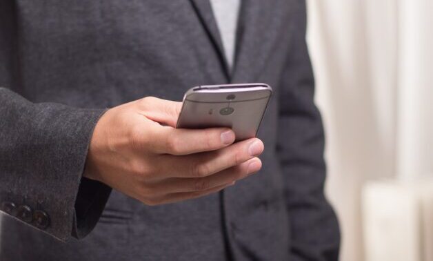 Photo of man in gray suit holding a cell phone. Close up of hand.
