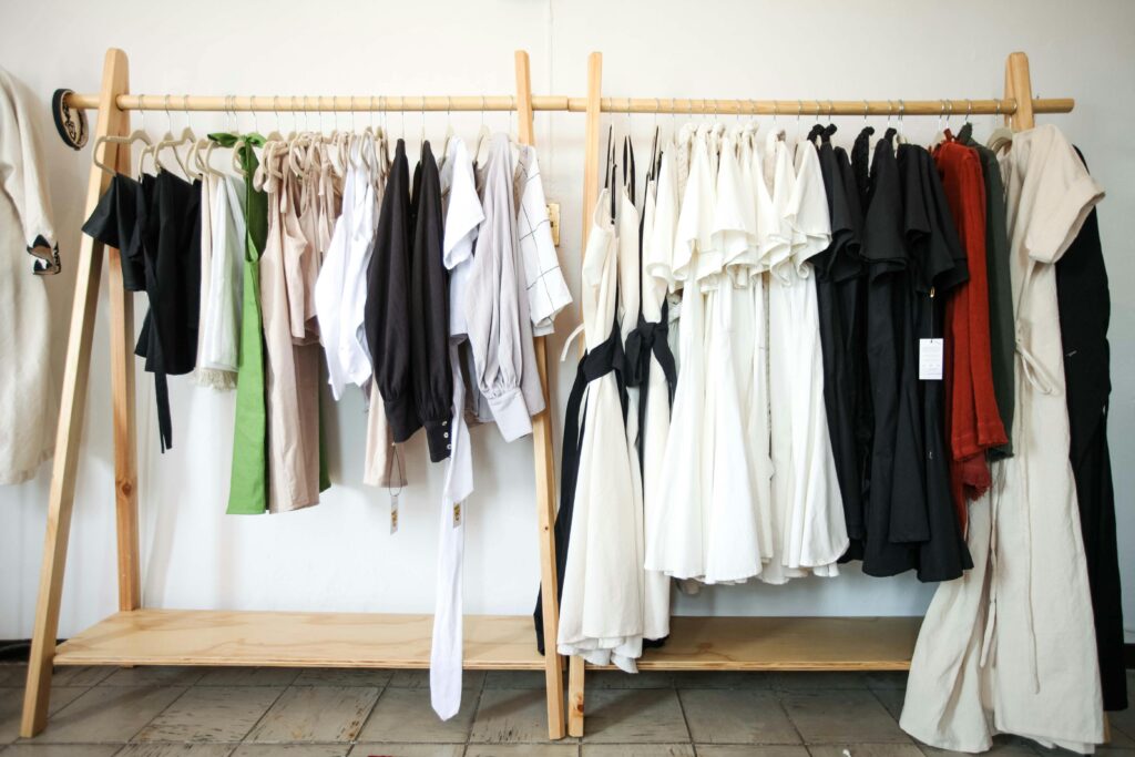 Close up of clothing rack with a variety of clothing hanging on it. Clothing rack is brown.