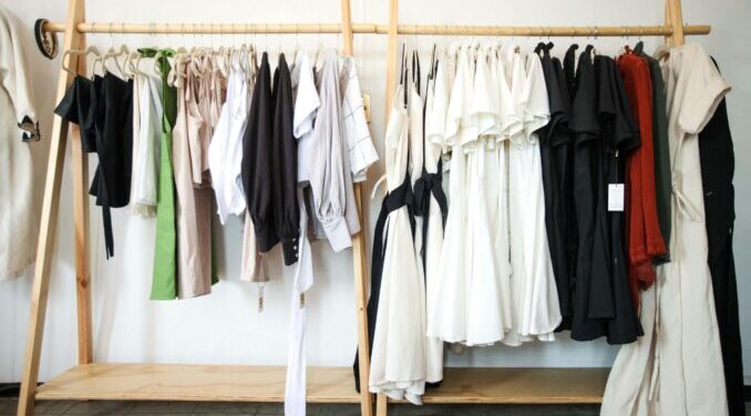 Close up of clothing rack with a variety of clothing hanging on it. Clothing rack is brown.