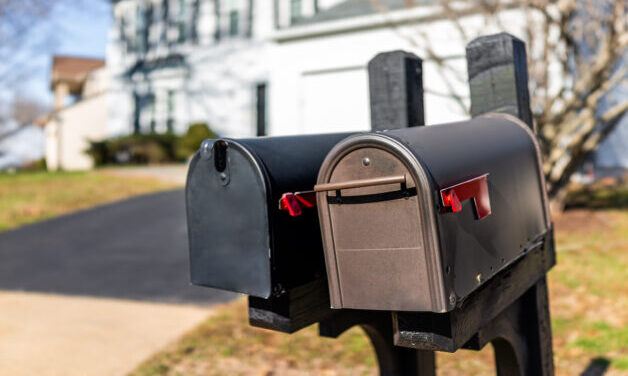 Closeup of two modern black and brown metal red flag mailboxes at single family home in residential suburbs with nobody and house in background