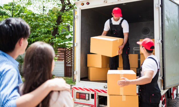 Asian and Caucasian workers in uniform unloading cardboard boxes from the truck. Delivery men unloading boxes and check the checklist with their coworkers. Professional delivery and moving service.