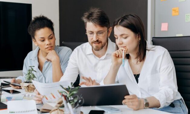 Group of people sitting around a table looking at a computer.